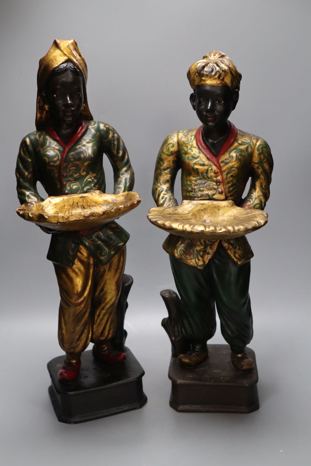 A pair of gilt and polychrome painted Nubian butlers, portrayed holding shell shaped trays